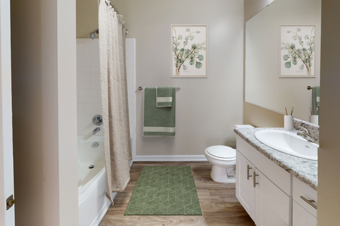 An apartment living room with a black leather chair next to a fireplace, windows, a ceiling fan, flat screen tv, and a white couch